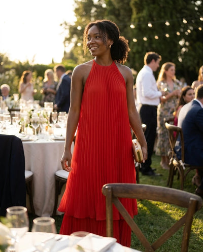 Woman in a red pleated halter midi dress at an outdoor wedding reception