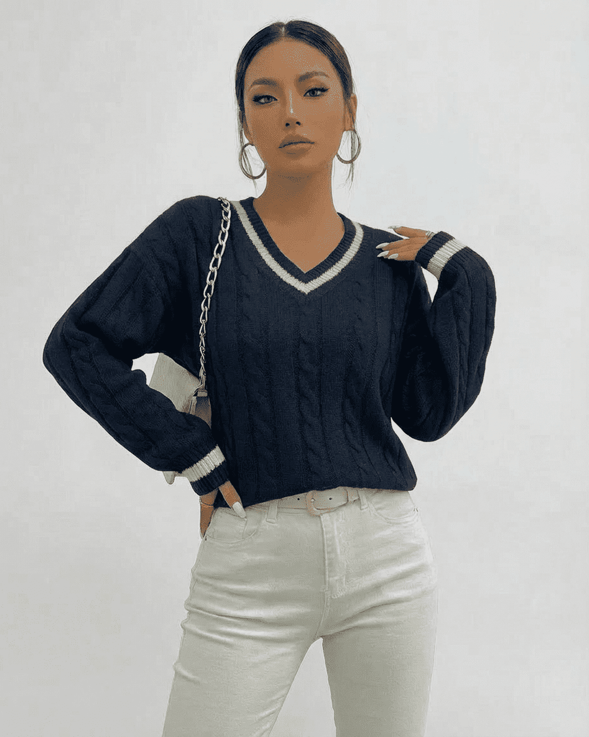 Marina Sweater in navy cable knit with V-neck, paired with white jeans, showcasing a modern casual look.