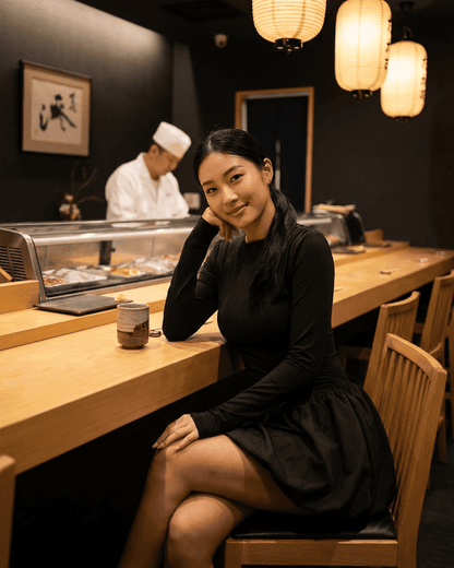 Elara Mini Dress by RAMBLION worn by a woman sitting at a sushi bar, featuring long sleeves and a tiered skirt.