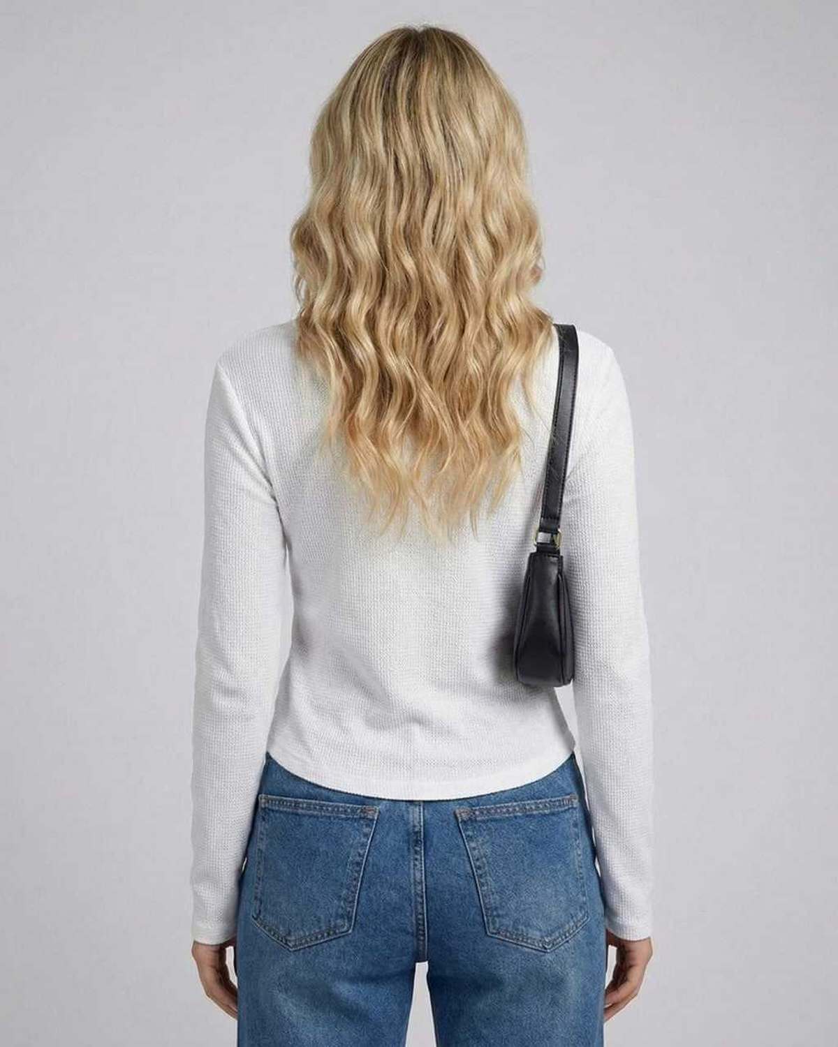 Back view of a woman in a Gand Top, white long sleeve with a round neckline, paired with denim jeans, by RAMBLION.