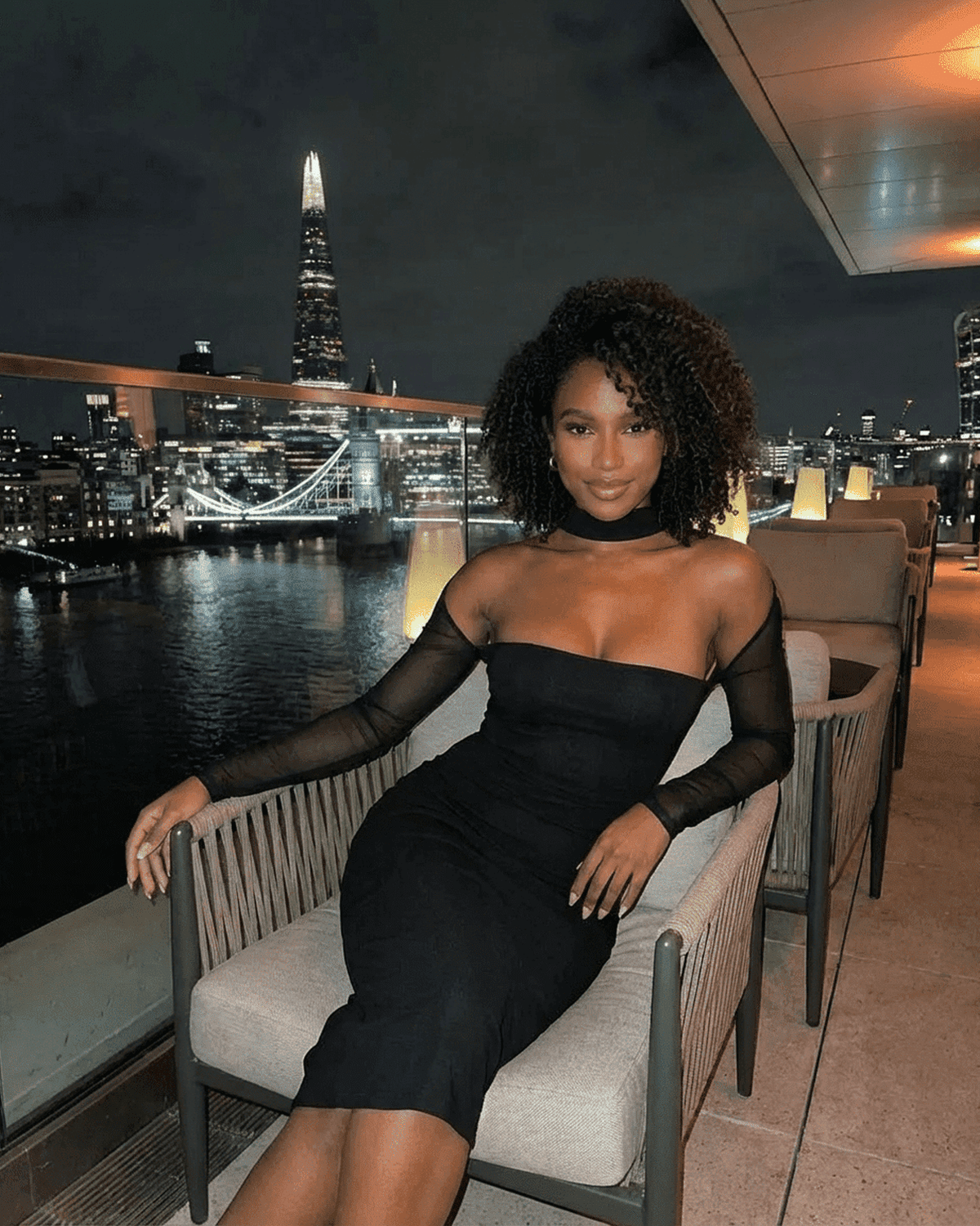 Model wearing the Arden Midi Dress by RAMBLION, showcasing a sleek silhouette and stylish cutout detail against a city skyline.
