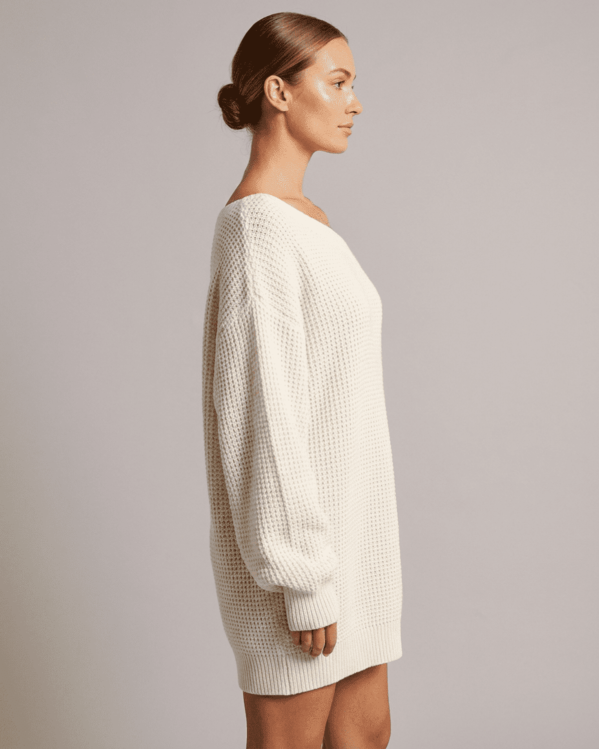 Side view of a woman wearing the RAMBLION Aurora Mini Dress, featuring a cozy white ribbed knit design.