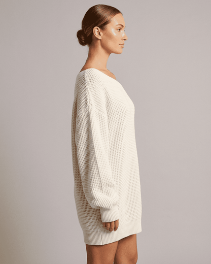 Side view of a woman wearing the RAMBLION Aurora Mini Dress, featuring a cozy white ribbed knit design.