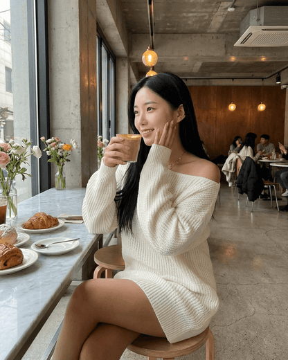 Woman enjoying a beverage in a cafe wearing the Aurora Mini Dress by RAMBLION, featuring an off-the-shoulder design.