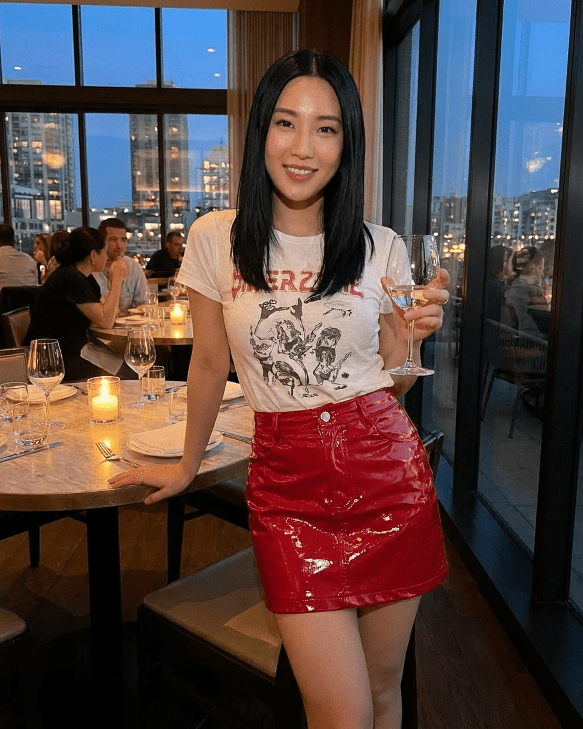 Woman in a restaurant wearing a Crimson Mini Skirt by RAMBLION, holding a drink, with city skyline in the background.