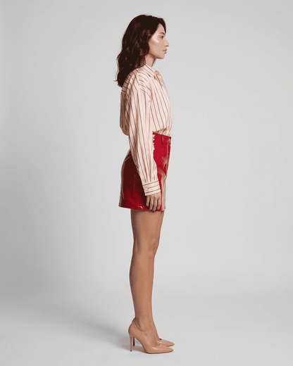 Side view of a model wearing a high-waisted Crimson Mini Skirt by RAMBLION, featuring a striking red glossy finish.