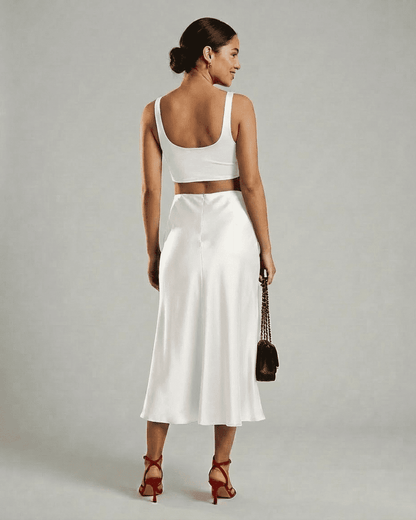 Woman in white back view wearing RAMBLION Luna Midi Skirt and cropped top, showcasing elegant satin mermaid design.