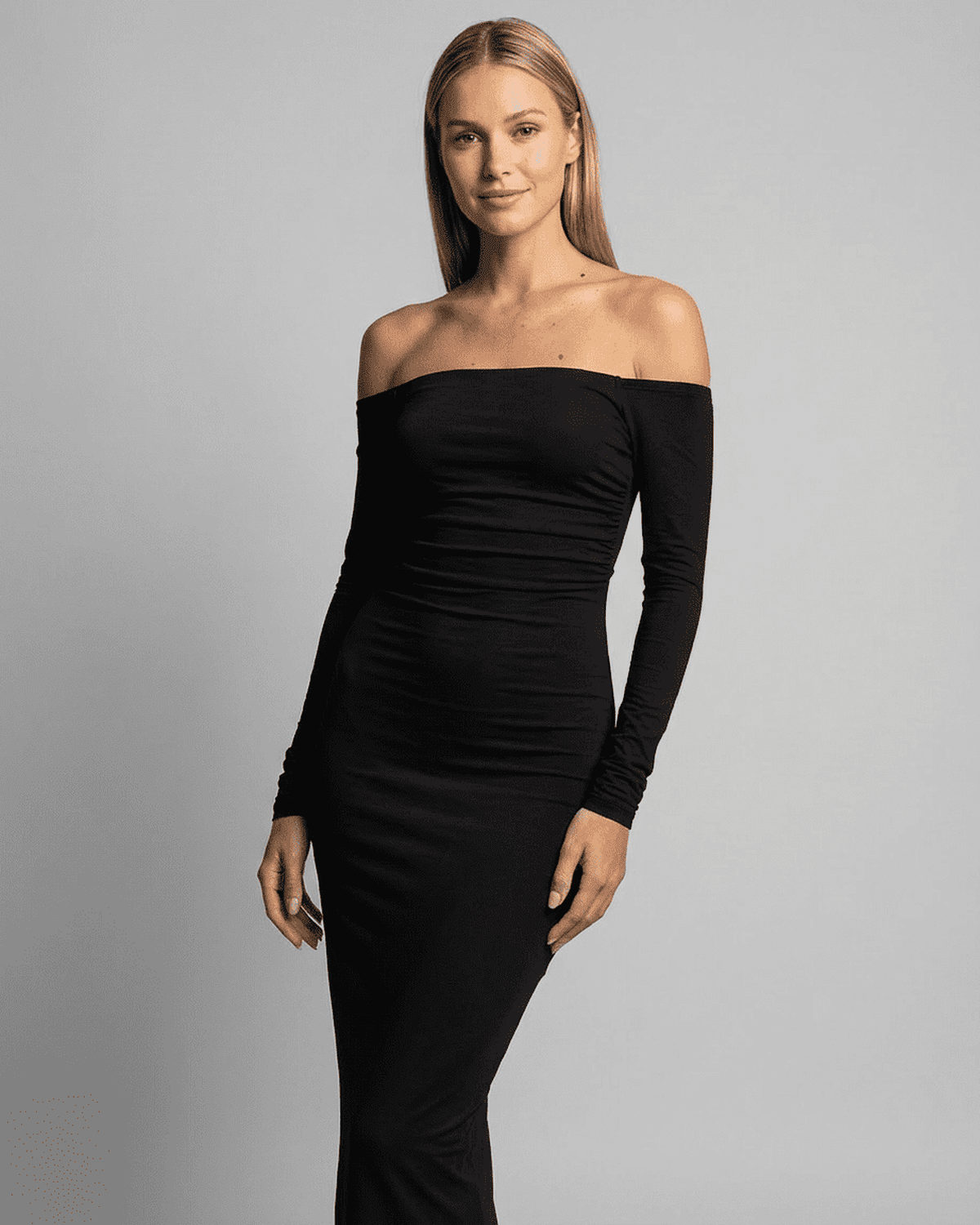 Elegant woman modeling the RAMBLION Nocturne Maxi Dress with off-shoulder slash neck and long sleeves.