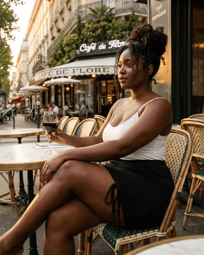 Woman enjoying a drink in Paris wearing a Noir Mini Skirt from RAMBLION, highlighting its high-waisted, bodycon silhouette.