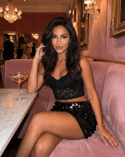 Obsidian Mini Skirt by RAMBLION worn by a model in a stylish setting with a drink, showcasing black sequin hem bodycon design.