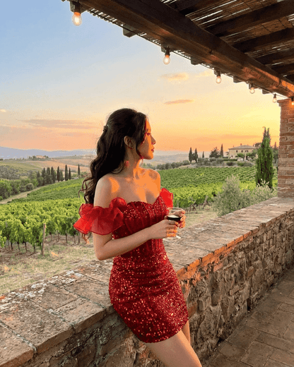 Scarlett Mini Dress by RAMBLION featuring a red sequin off-the-shoulder design against a scenic sunset.