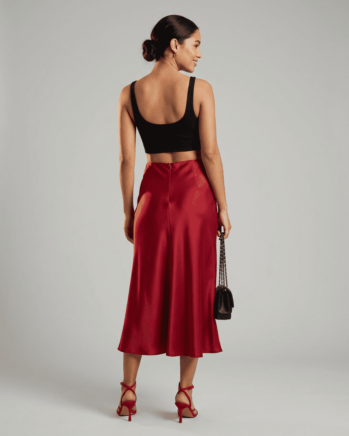 Back view of a model wearing the Rosalia Midi Skirt by RAMBLION, showcasing its elegant satin mermaid design in rich red.