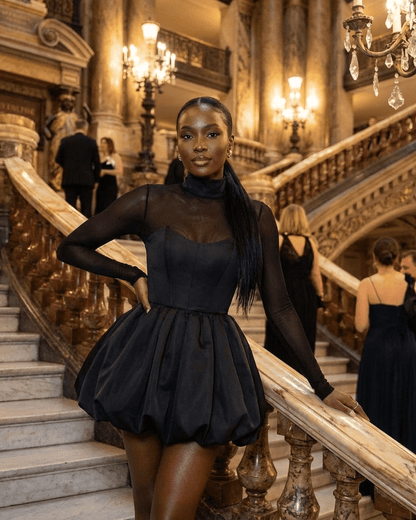 Elegant model wearing Selene Mini Dress by RAMBLION with a bubble hem, posing on grand stairs in an upscale venue.