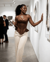 Model wearing Sienna Corset Top in brown, showcasing its sophisticated satin structure at an art gallery.