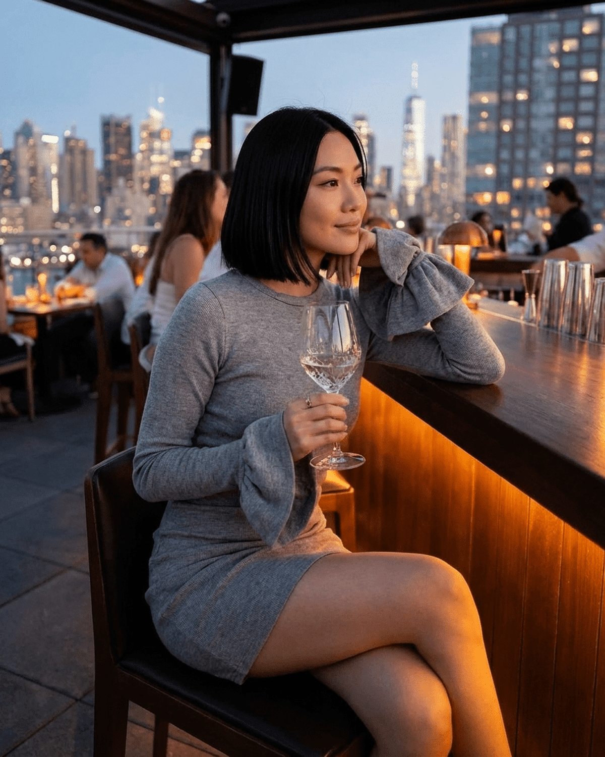 Woman wearing Luna Mini Dress with ruffled sleeves, enjoying a drink at a rooftop bar.