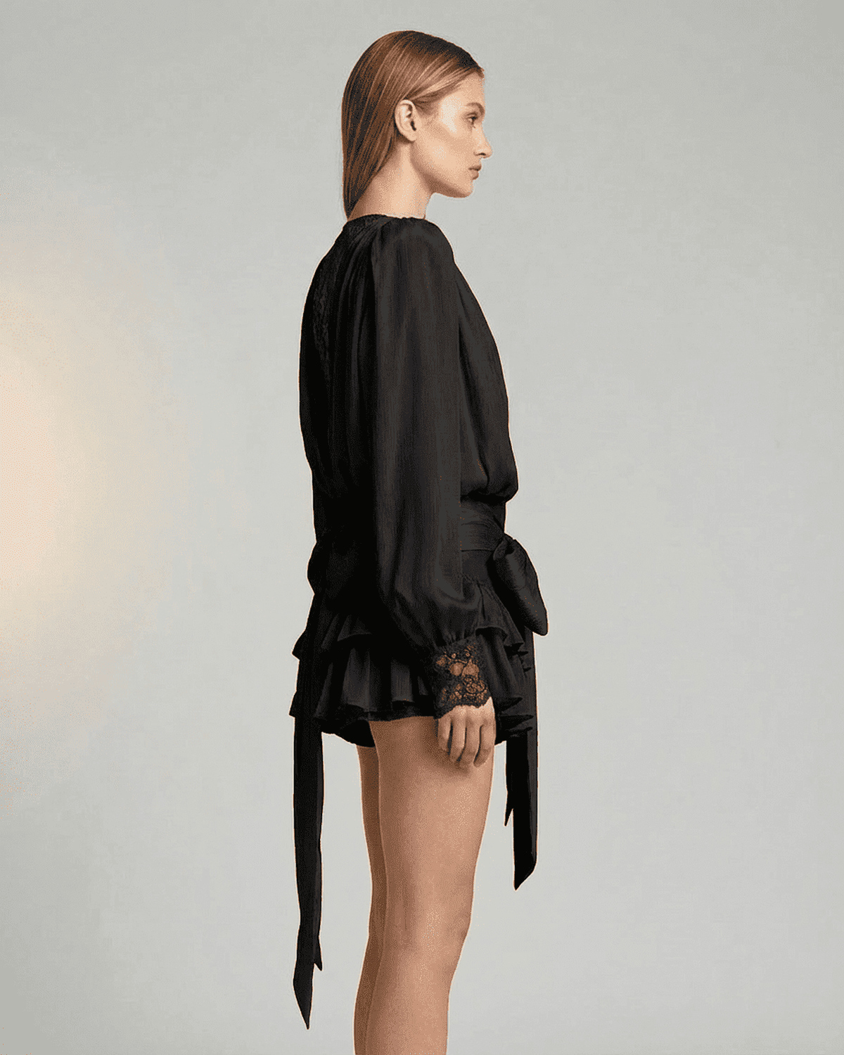 Side view of a model wearing the RAMBLION Noir Mini Dress with lace detail and long sleeves.