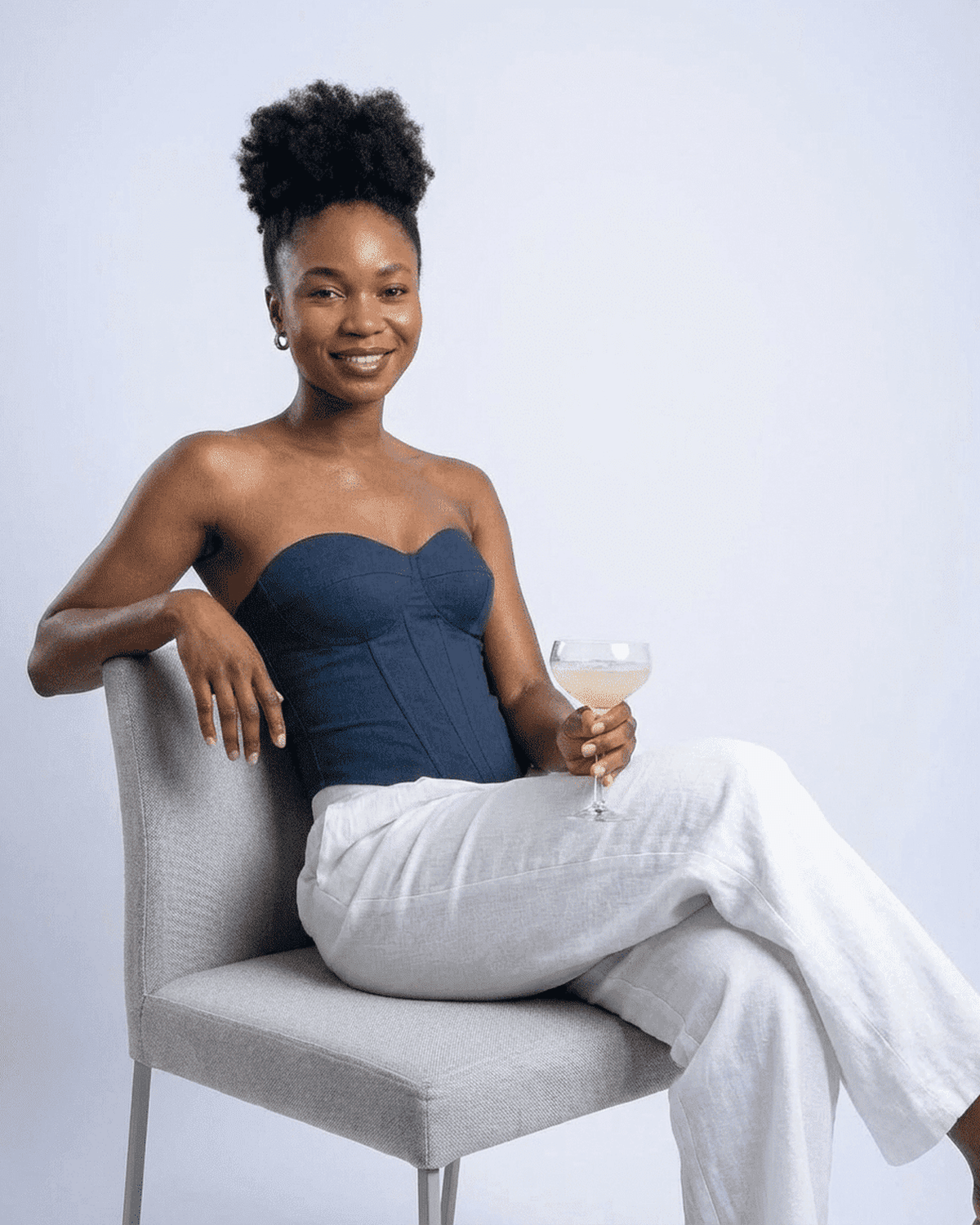 Model wearing Atlas Corset Top, a navy faux denim bustier, seated with a cocktail in hand.