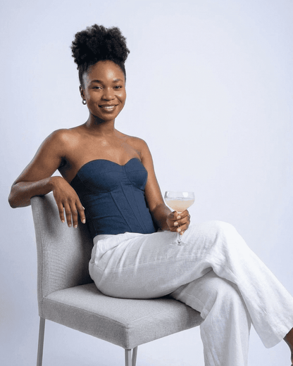 Model wearing Atlas Corset Top, a navy faux denim bustier, seated with a cocktail in hand.