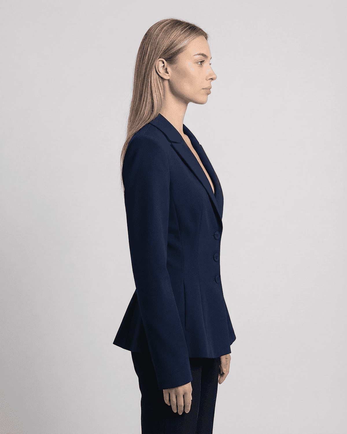 Profile view of a woman wearing the Aurora Blazer by RAMBLION, showcasing its fitted waist and sharp V-neckline.