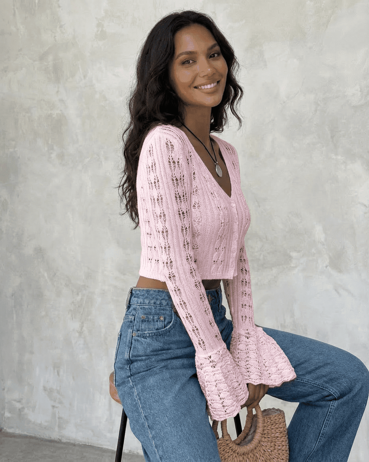 Woman wearing a pink Blossom Cardigan with flare sleeves, paired with high-waisted jeans.