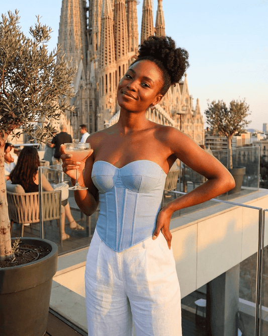 Denali Corset Top worn by a woman with a cocktail, against a beautiful backdrop, showcasing modern denim style.