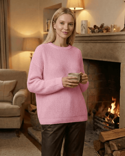 Fiora Sweater in pink, loose fit thick ribbed knitwear with round neck, cozy style near a fireplace.