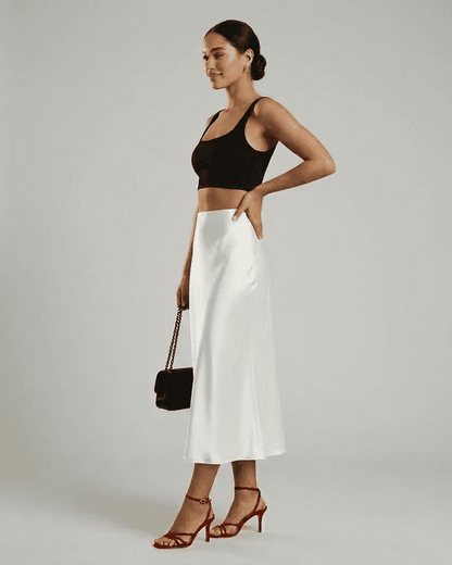 Model wearing the Luna Midi Skirt, a satin mermaid skirt in white, paired with a black crop top and red heels.