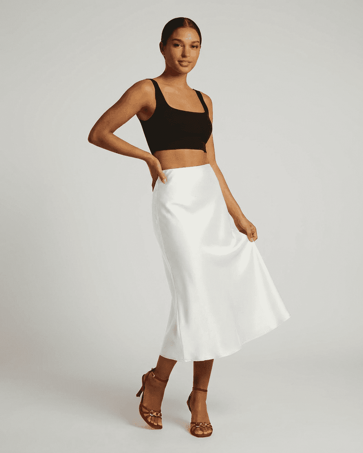 Model showcasing the Luna Midi Skirt, a satin mermaid midi skirt in white, paired with a black crop top.