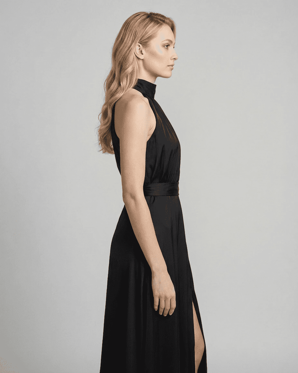 Profile view of Noctis Maxi Dress, a sleek black sleeveless turtleneck dress by RAMBLION with high waist and side slit.