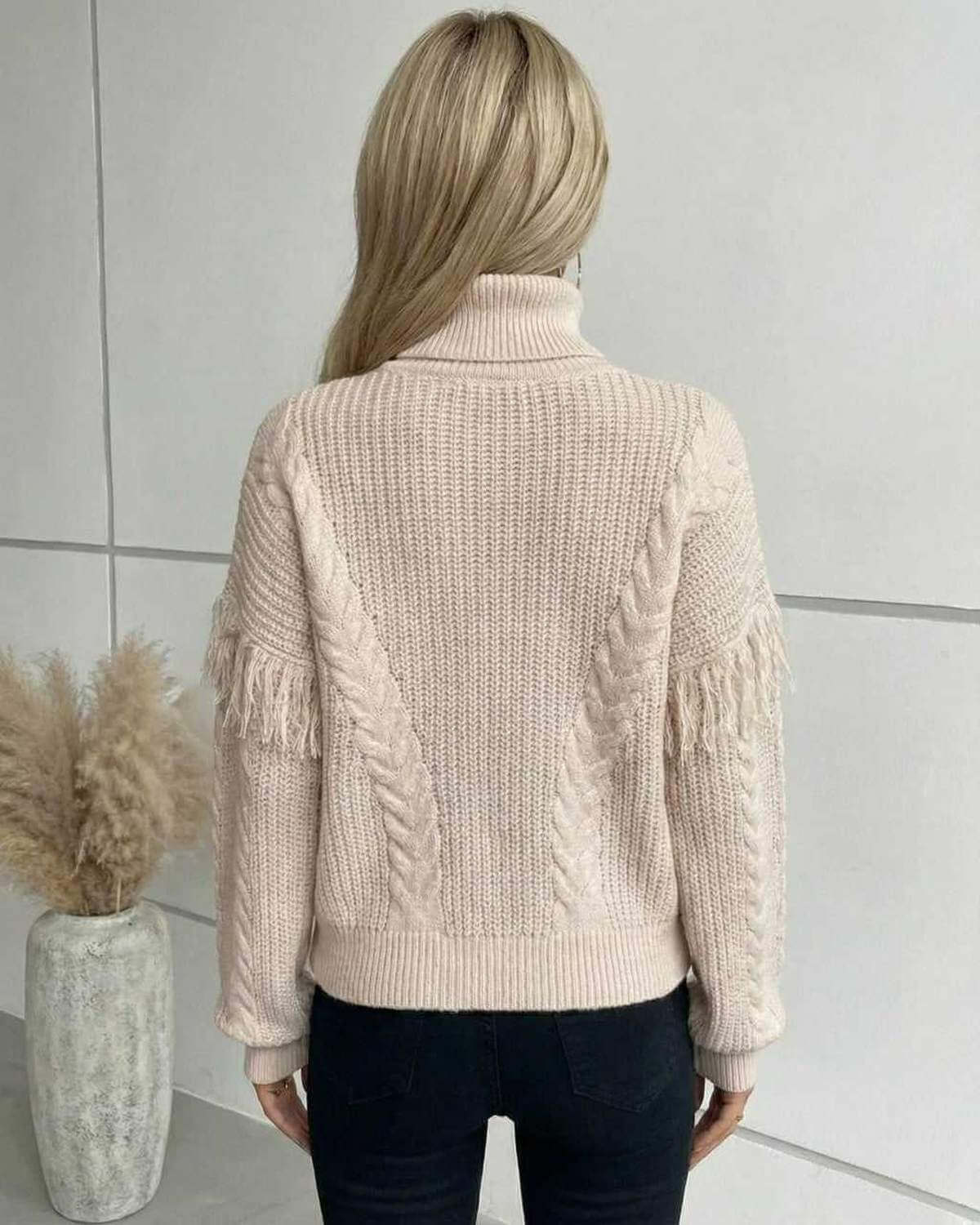 Back view of a woman wearing the RAMBLION Vienna Sweater, a beige cable knit turtleneck with fringe detailing.