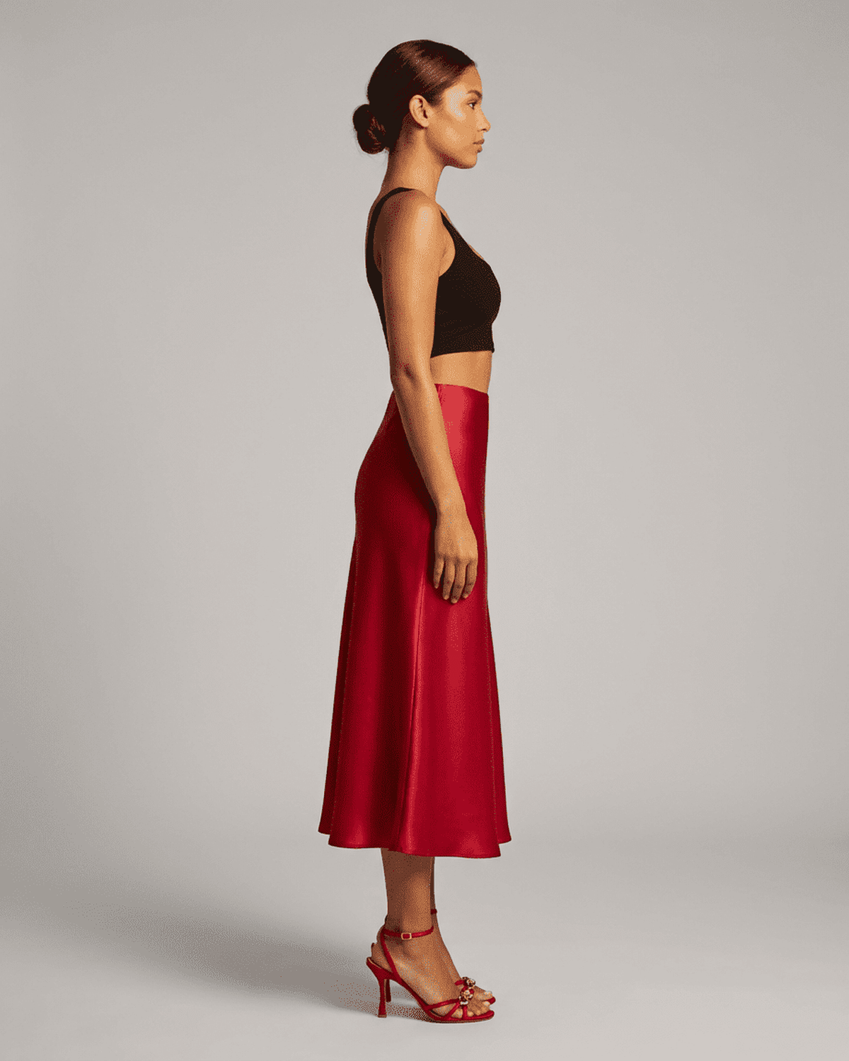 Side view of a woman wearing the Rosalia Midi Skirt by RAMBLION in rich red satin, showcasing its elegant silhouette.