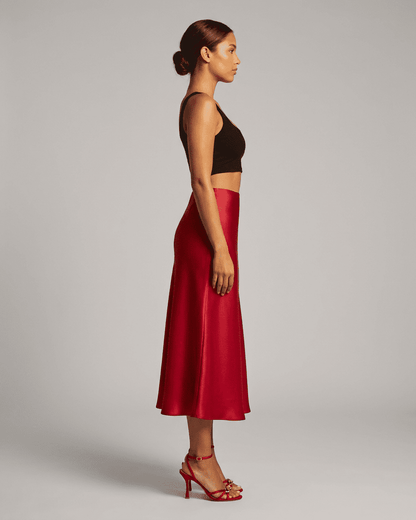 Side view of a woman wearing the Rosalia Midi Skirt by RAMBLION in rich red satin, showcasing its elegant silhouette.