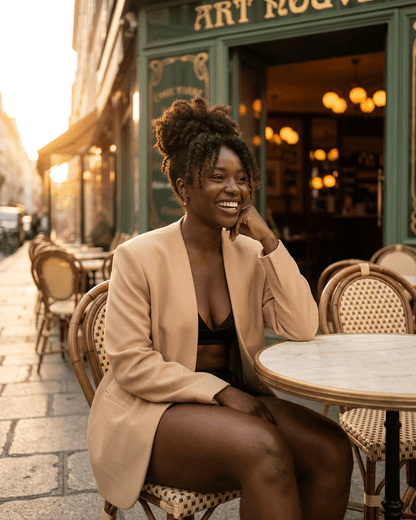 Savona Blazer by RAMBLION worn by a woman sitting at a café, showcasing a modern tailored silhouette in beige.