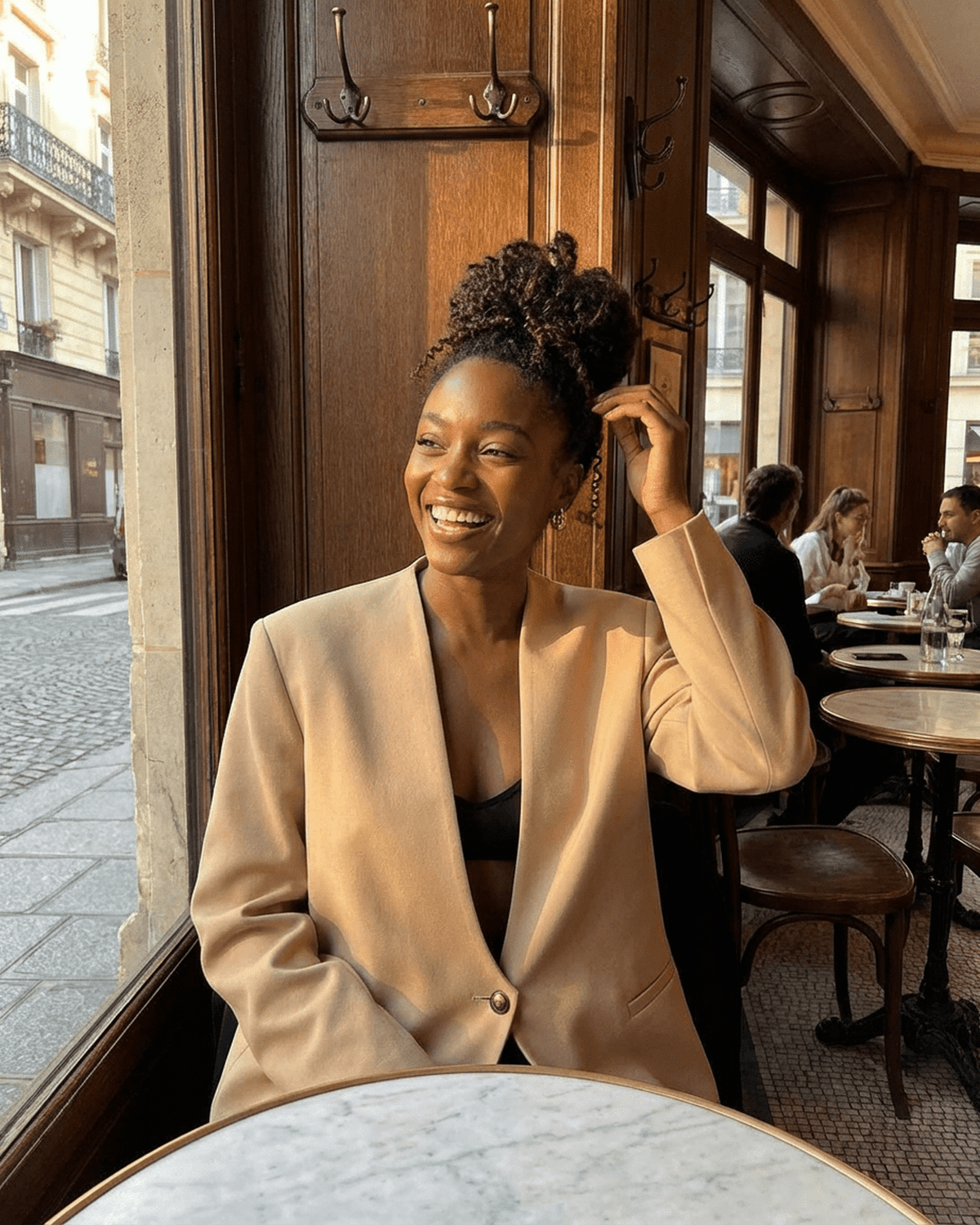 Savona Blazer by RAMBLION worn by a smiling woman in a café setting, showcasing a chic, tailored look.