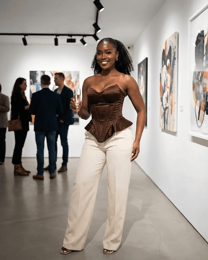Sienna Corset Top in rich brown satin worn by a woman at an art gallery event, showcasing sophistication and elegance.