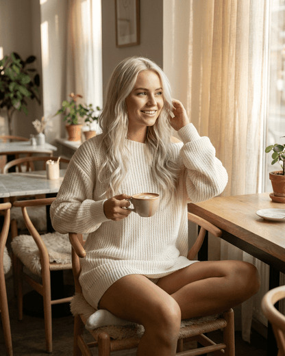 Aurora Mini Dress by RAMBLION, white ribbed knit off-the-shoulder style worn in a cozy cafe setting.