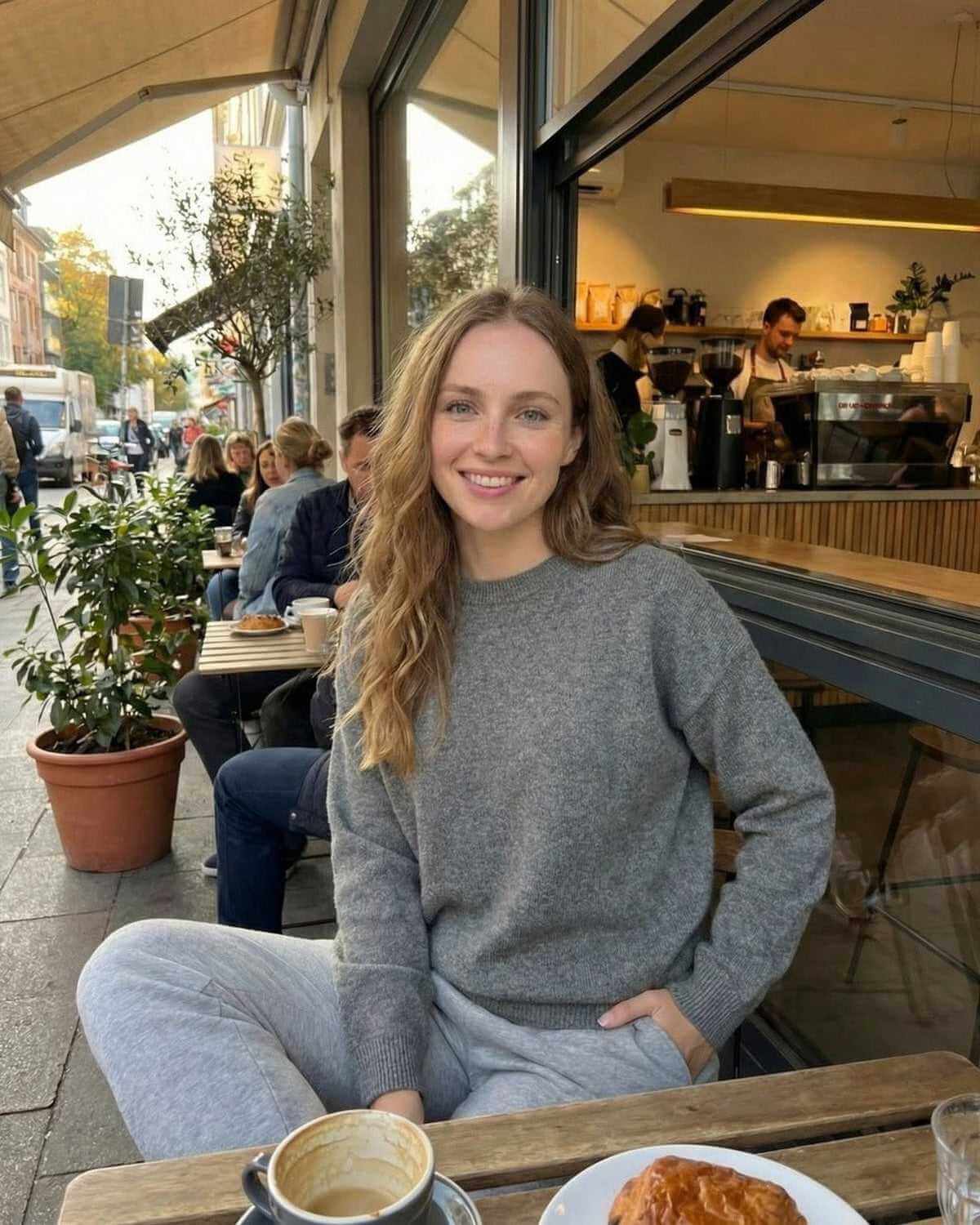 Wyra Pullover in grey worn by a woman at a café, showcasing comfort and style perfect for cozy outings. RAMBLION.